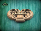 a carved wooden piece with an intricate, swirling design on a green background.