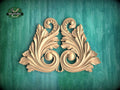 a decorative wooden carving of two ornate leaves or flowers, with intricate scrollwork and a symmetrical design, set against a green background.
