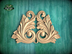 a decorative wooden carving of two ornate leaves or flowers, with intricate scrollwork and a symmetrical design, set against a green background.