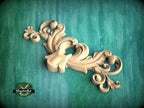 A decorative wooden carving in the shape of a stylized flower or plant is displayed against a teal background.
