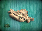 A wooden carving of a leaf-like design is displayed against a green background.