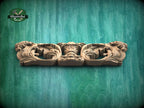 A carved wooden piece with intricate floral designs is displayed against a green background.