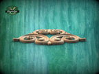 A decorative wooden carving with intricate scrollwork is displayed against a textured green background.