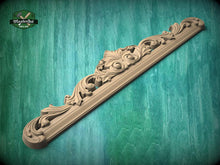 Load image into Gallery viewer, A decorative wooden carving or panel with intricate floral and scrollwork designs, resting on a green wooden surface.
