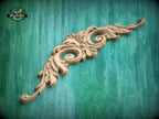 A decorative wooden carving with intricate scrollwork is displayed against a green wooden background.