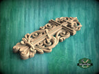 A decorative wooden carving with intricate floral and scrollwork designs is displayed against a green background.