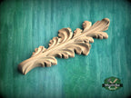 A wooden carving of a leaf-like design is displayed against a green background.