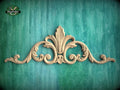 A decorative wooden carving with an ornate, floral-inspired design is displayed against a teal-colored background.