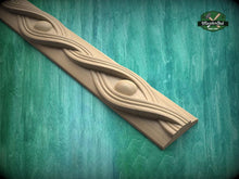 Load image into Gallery viewer, A wooden carving with a curved design and a central eye-shaped element is displayed against a green background.
