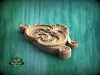 A wooden carving with intricate scrollwork and floral designs is displayed against a green background.