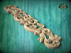 A decorative wooden carving with intricate scrollwork and floral patterns is displayed against a teal background.