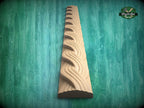A wooden carving of a curved, wavy design is displayed against a green background.