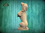 A wooden sculpture of a dog sitting upright on its hind legs, positioned against a green background.