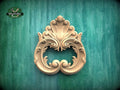 an ornate, carved wooden piece with intricate scrollwork and floral designs, set against a green textured background.