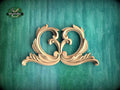 a decorative wooden carving of two ornate, curving shapes on a green background.