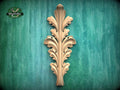 a decorative wooden leaf-like object with a vertical, ornate design on a green background.