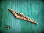 A wooden carving or sculpture with intricate floral designs is displayed against a green textured background.