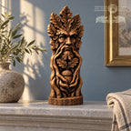 A wooden sculpture of a face with a leafy beard and an acorn in its mouth, placed on a marble surface.