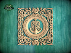 a square, ornately carved wooden frame with a central anchor and floral designs surrounding it, set against a teal background.