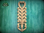 a decorative wooden carving of a stylized tree or plant with intricate scrollwork and shapes, mounted on a green textured background.